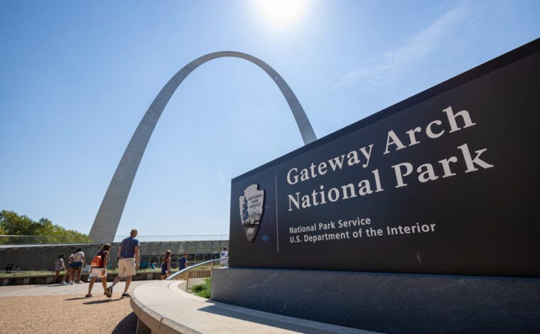 Visitors walking into the visitor center entrance at Gateway Arch National Park on a sunny summer day.